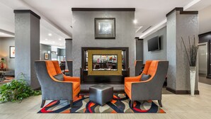 A lobby with two grey armchairs, a central ottoman, and a fireplace.