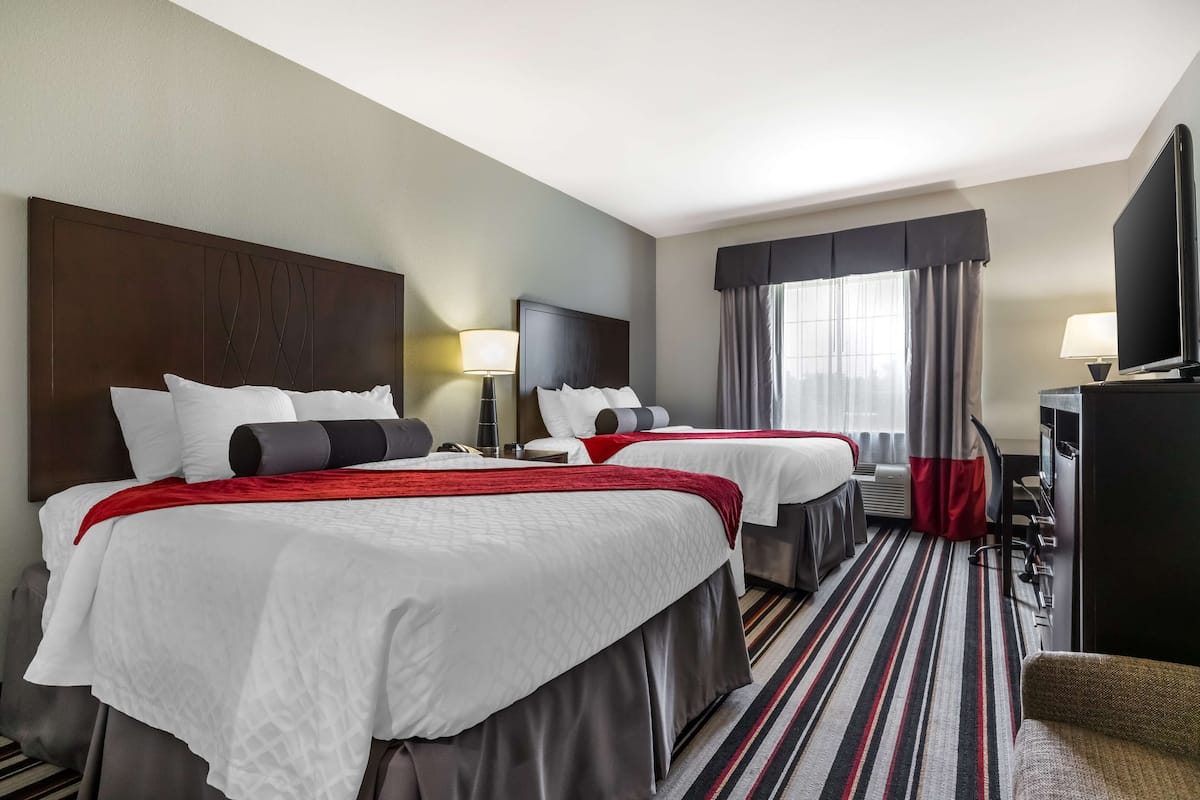 A hotel room with two beds, a television, a desk, and a window with curtains.