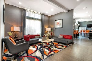 Una habitación de hotel moderna con un sofá gris, un sillón y una pequeña mesa de centro. Cuenta con un comedor con barra y sillas.