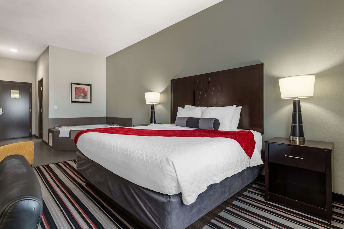 A hotel room with a large bed, two bedside tables with lamps, a red throw blanket, and a striped rug.