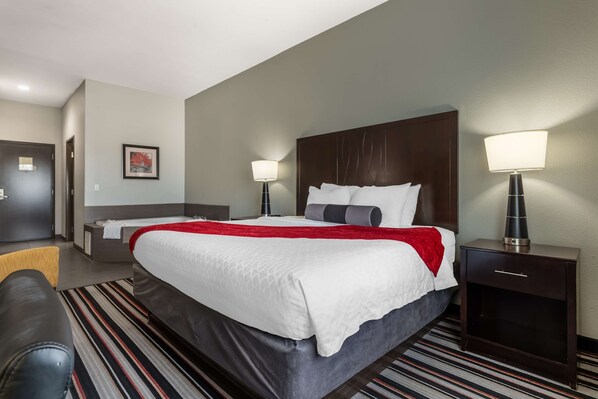 A hotel room with a large bed, two bedside tables with lamps, a red throw blanket, and a striped rug.