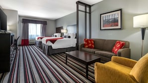 A hotel room with a bed, a sofa, a coffee table, a TV, and a painting on the wall.