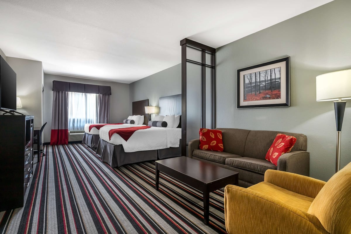A hotel room with a bed, a sofa, a coffee table, a TV, and a painting on the wall.