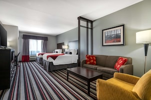 Una habitación de hotel con cama, sofá, mesa de centro, televisor y un cuadro en la pared.