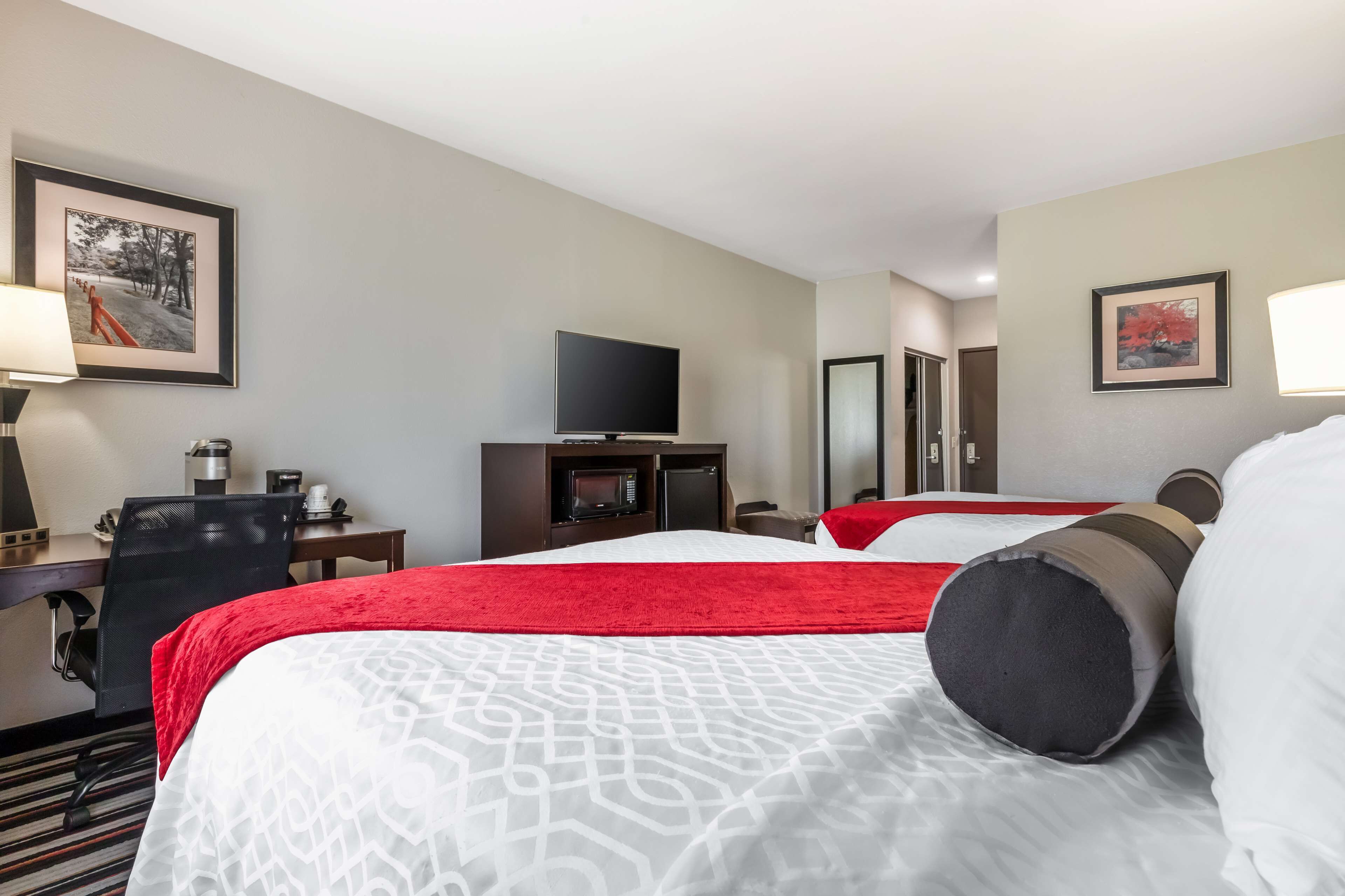 A hotel room with a large bed, a desk with a computer, a television, and two framed pictures on the wall.