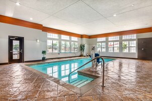 Una amplia piscina interior con agua cristalina y azul, rodeada de un suelo de baldosas y detalles de madera.