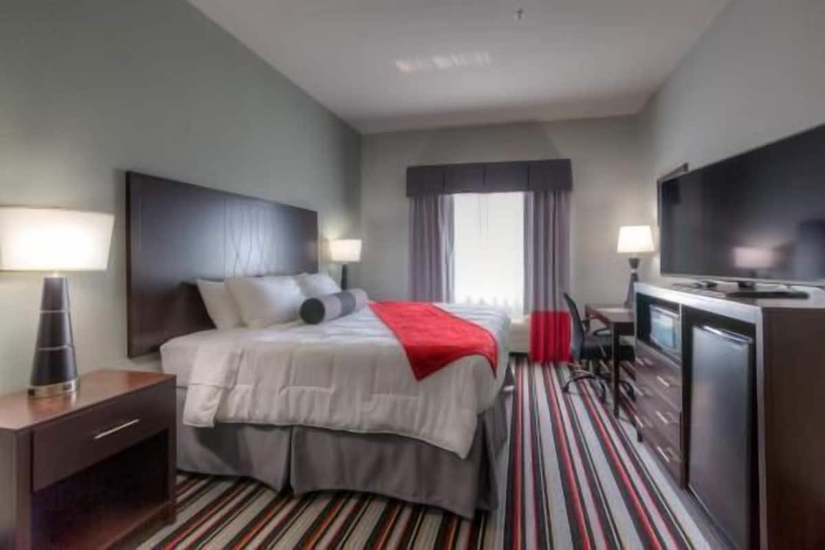 A hotel room with a bed, a desk, a TV, and a window.