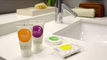 A bathroom with a white sink, two bottles of shampoo, a conditioner, and a soap bar.