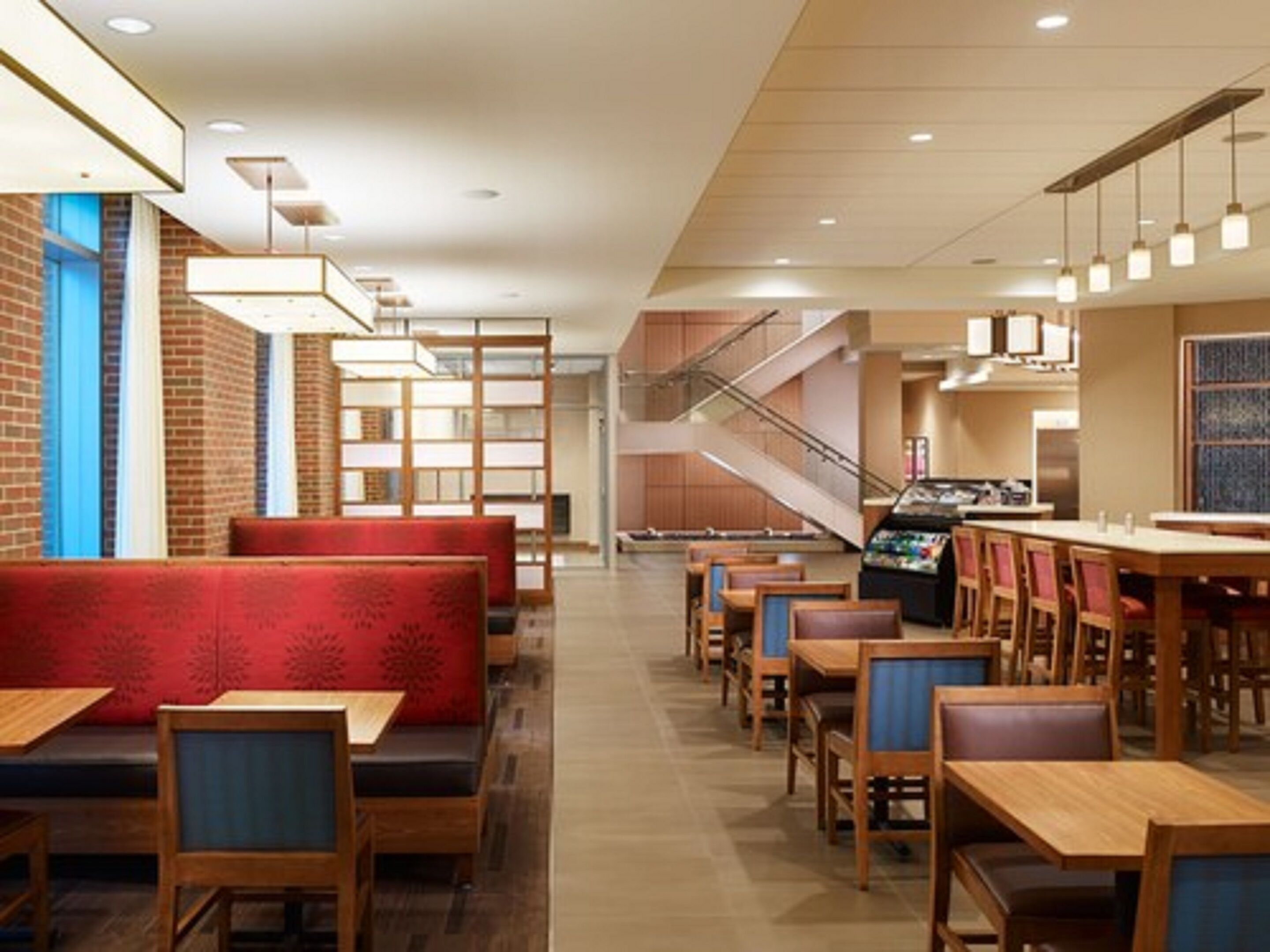 A modern restaurant with wooden tables and booths, a staircase, and a jukebox.