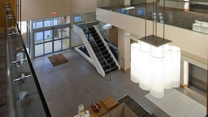 Un vestíbulo amplio con una escalera, barandilla de cristal y un moderno candelabro.