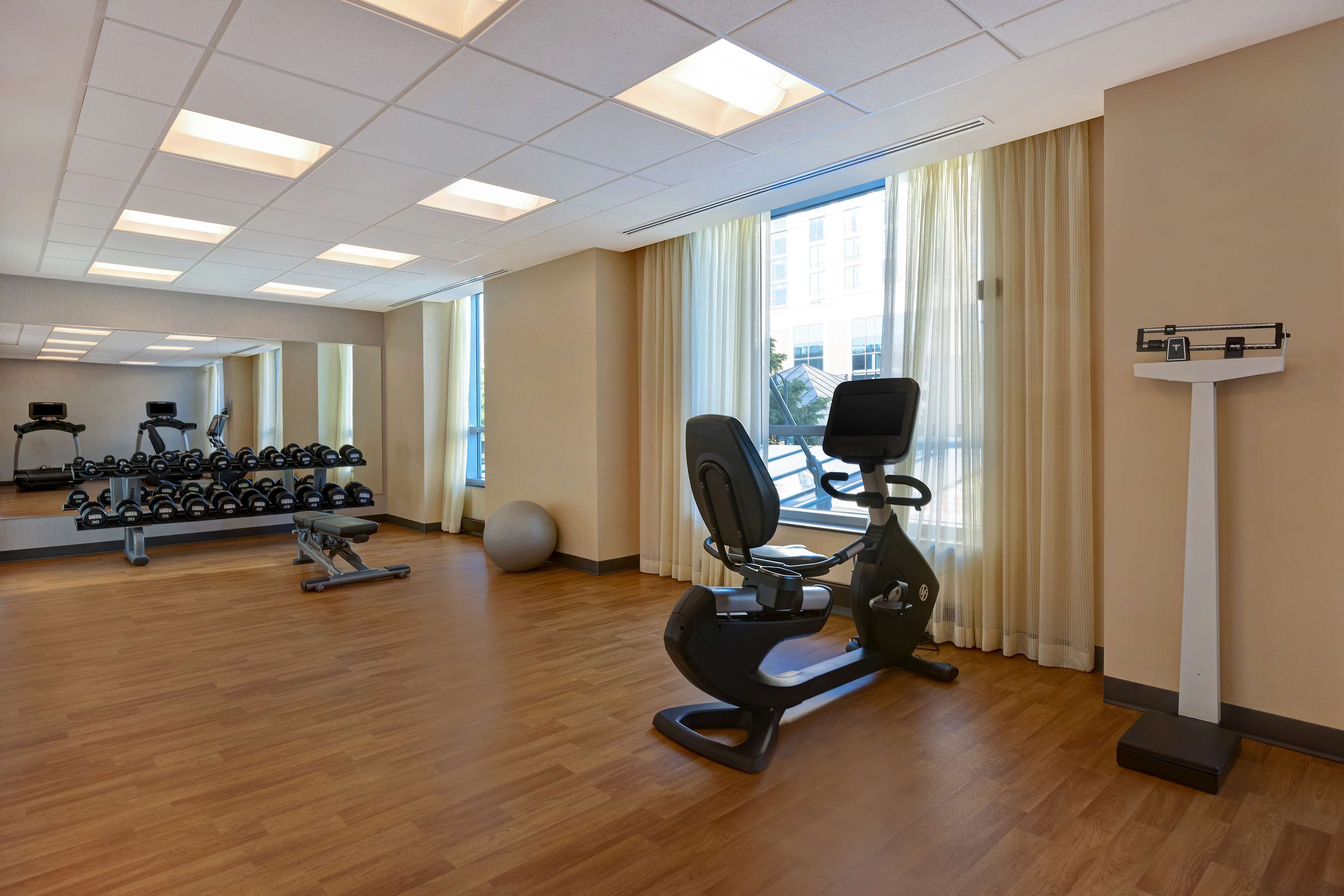 A gym with exercise equipment, a mirror, and a window with curtains.
