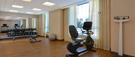 Un gimnasio con equipo de ejercicio, un espejo y una ventana con cortinas.