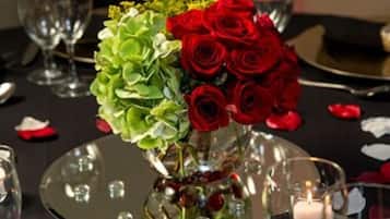 A table set for a formal event with a centerpiece of red roses and green foliage, surrounded by wine glasses and a candle.
