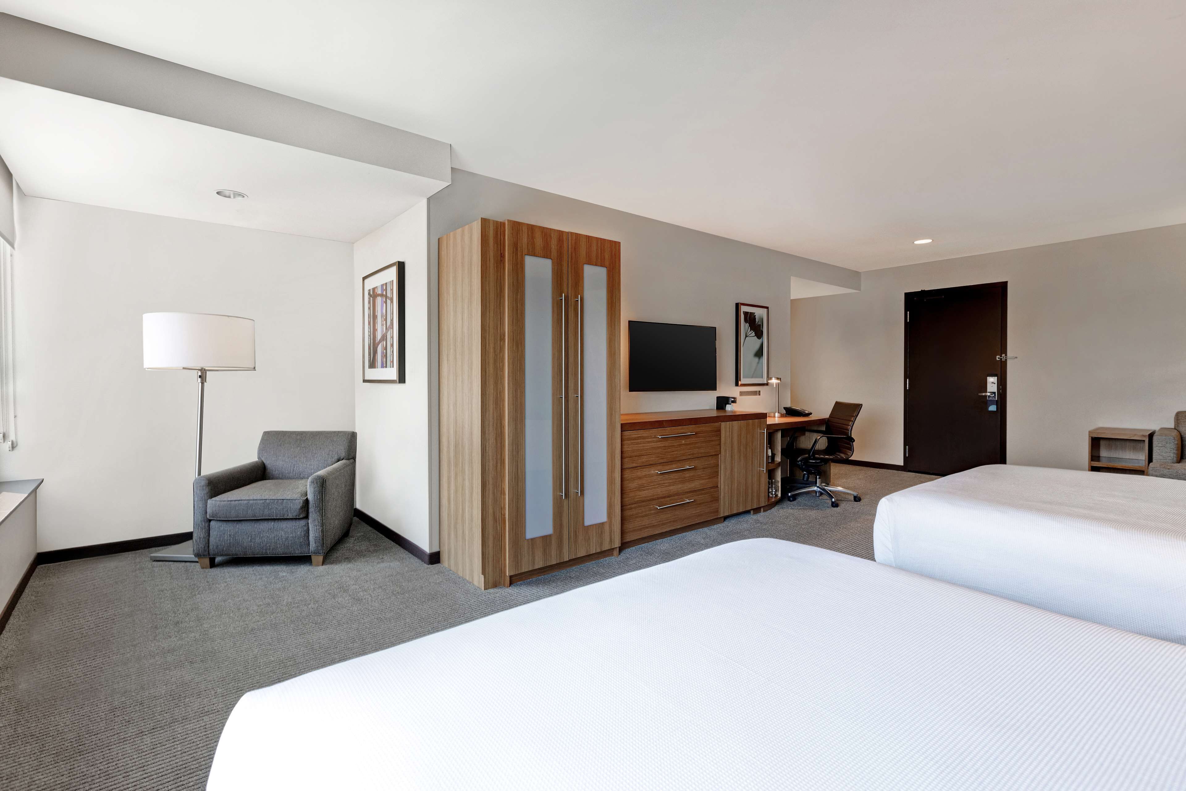 A hotel room with two beds, a desk with a chair, a wardrobe, a television, and a lamp.