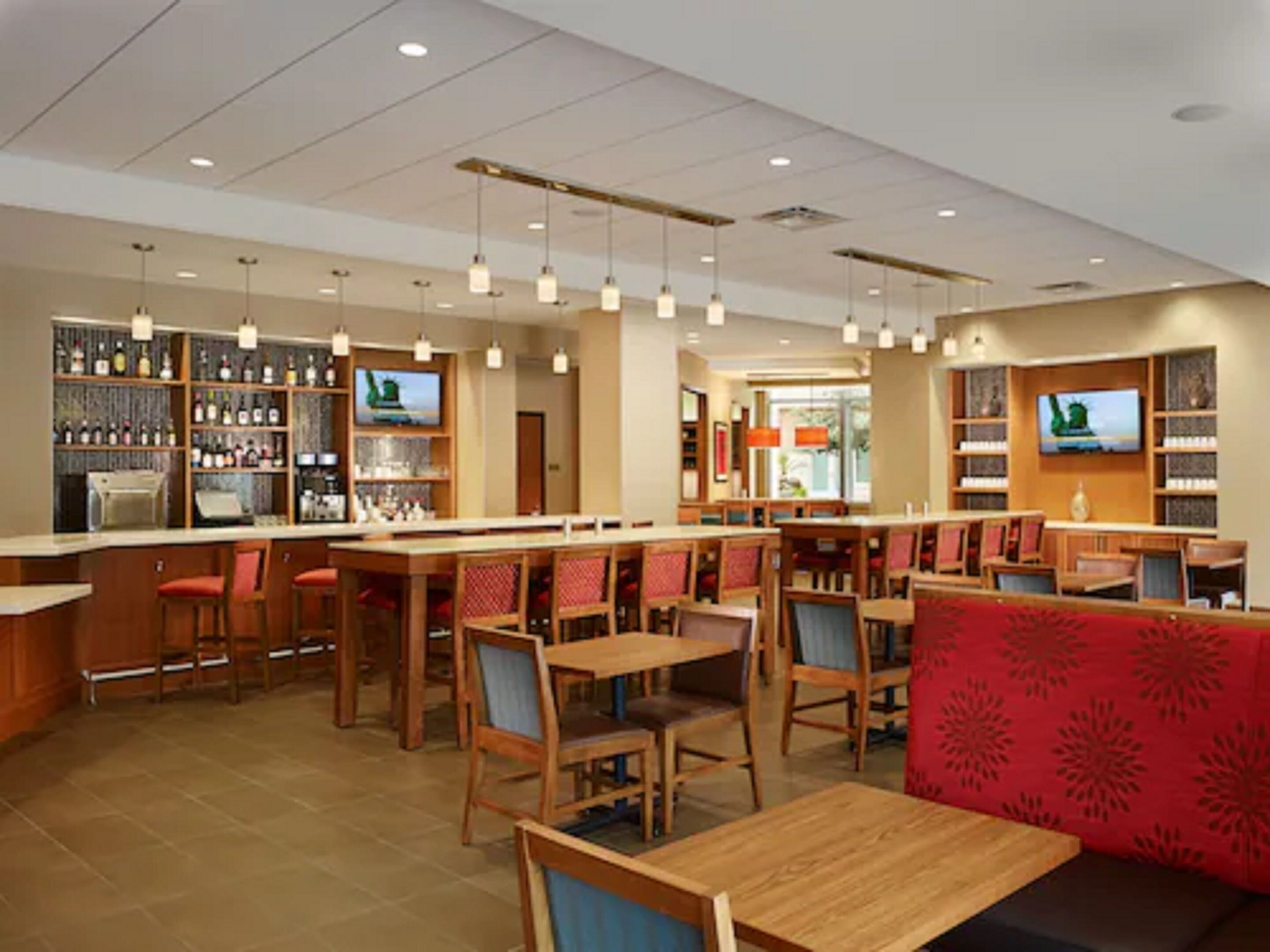 A restaurant with wooden tables and chairs, a bar area with shelves of bottles, and a television mounted on the wall.