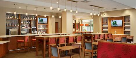 A restaurant with wooden tables and chairs, a bar area with shelves of bottles, and a television mounted on the wall.