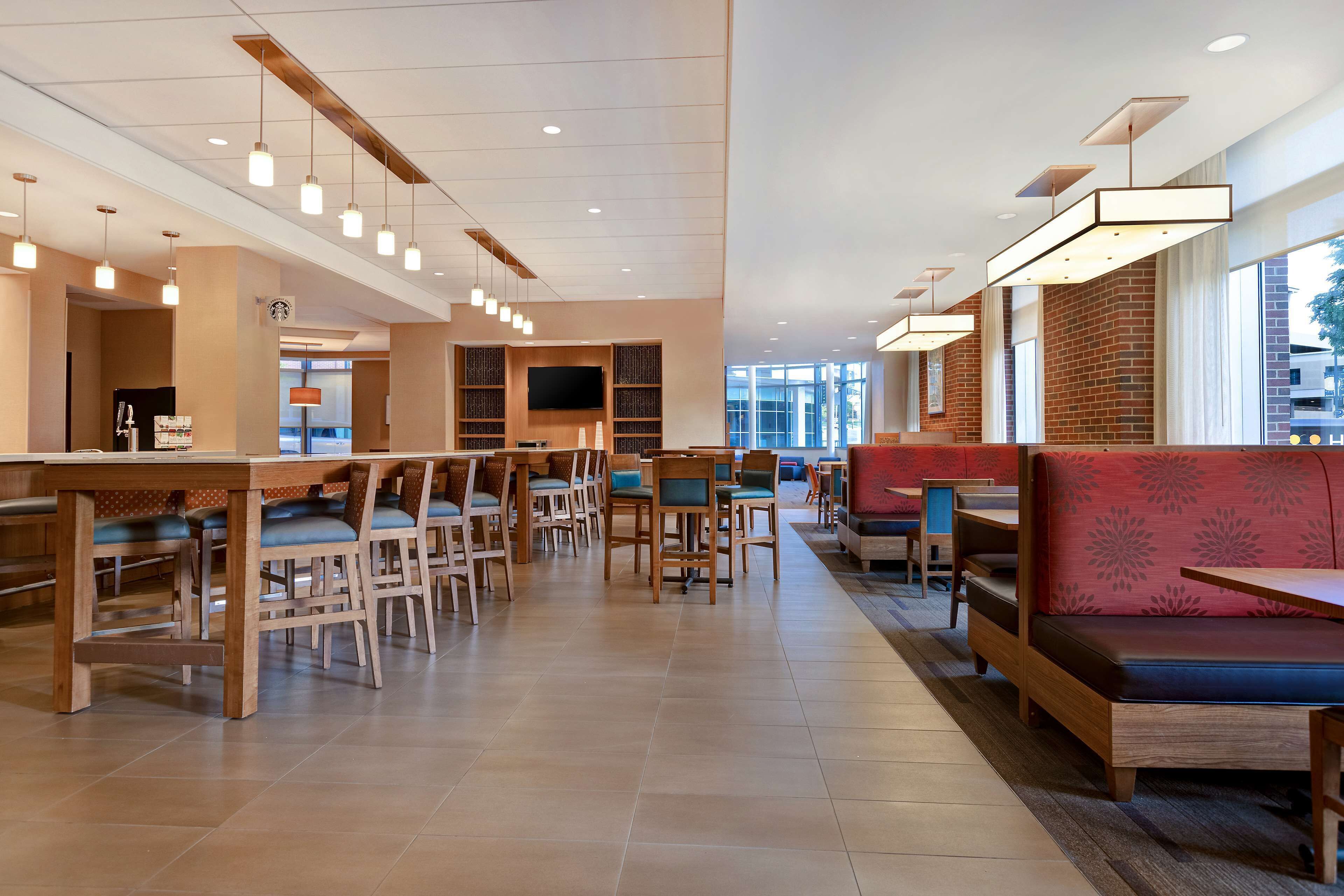 A spacious restaurant with multiple dining tables and chairs, a large TV screen, and a seating area with cushioned benches.