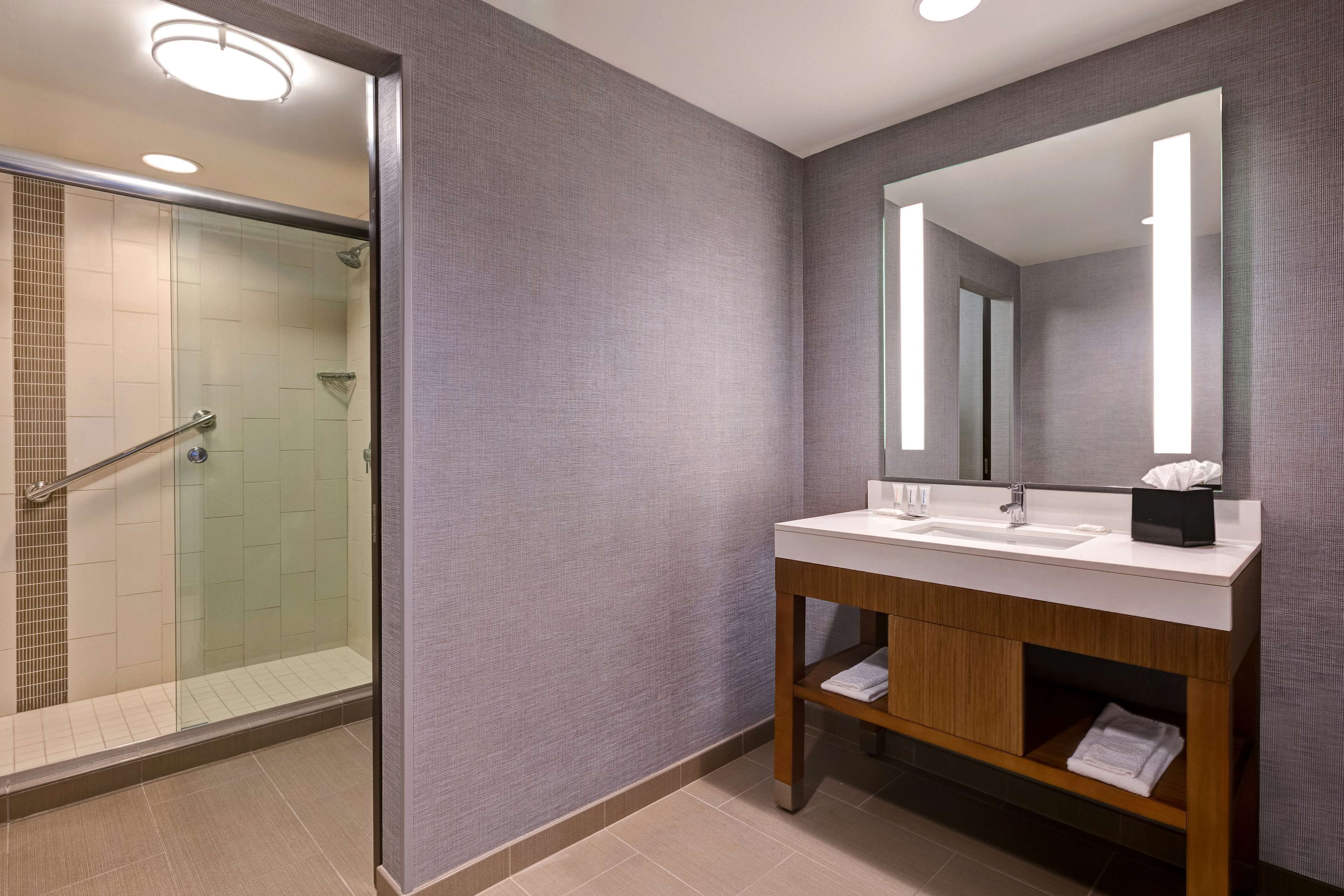Une salle de bain moderne avec une douche à parois de verre, un meuble-lavabo en bois avec un miroir et un lavabo blanc.