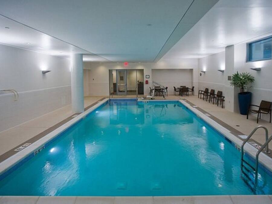 Piscina interior com água cristalina, cercada por cadeiras e um vaso de planta.