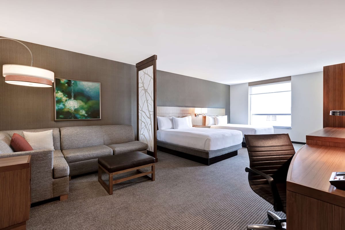 A hotel room with a bed, a sofa, a desk, and a large window.