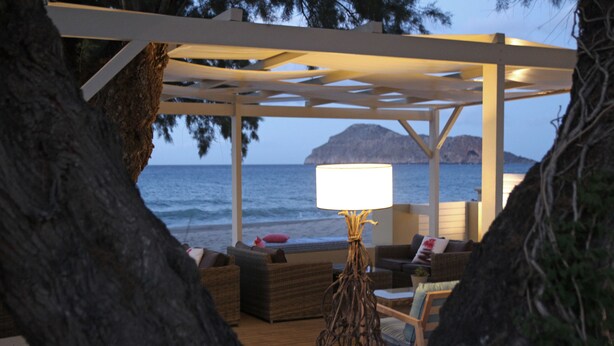 A covered outdoor seating area with a view of the sea, a lamp, and wicker furniture. - Effi Apartments (Platanias)