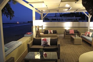 Cómoda zona de estar al aire libre con muebles de mimbre y cojines, con vista a una playa al atardecer.