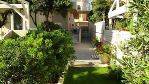 A narrow pathway flanked by greenery and modern buildings, leading to a covered outdoor area. - Effi Apartments (Platanias)