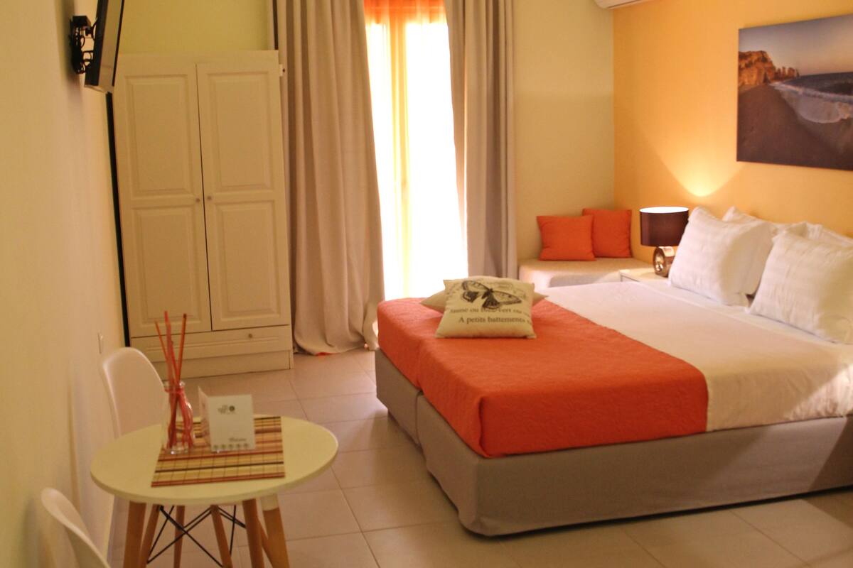 A hotel room with a bed, a desk with a chair, a table, and a wardrobe.