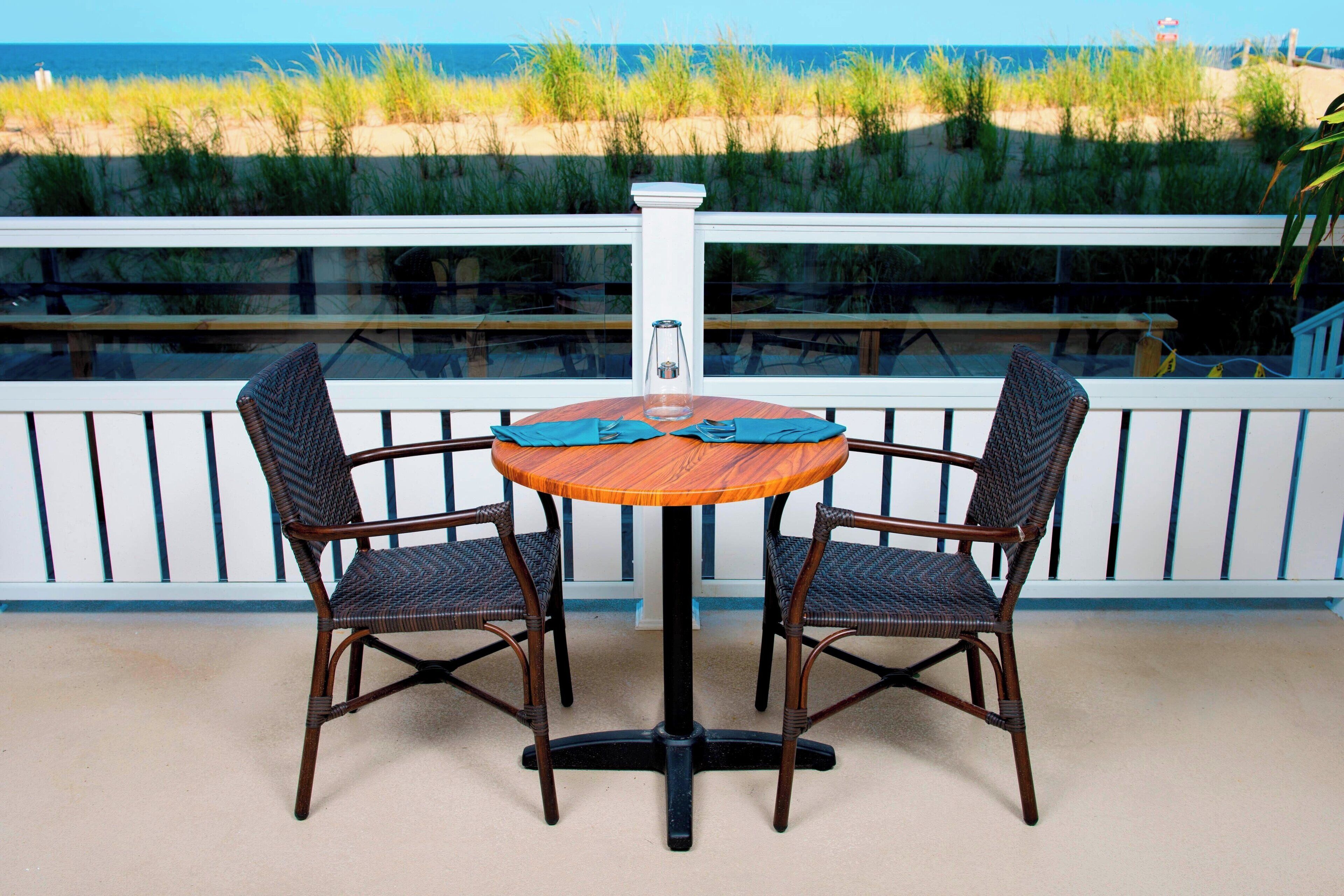 A round wooden table with two wicker chairs, a glass vase, and a bench.