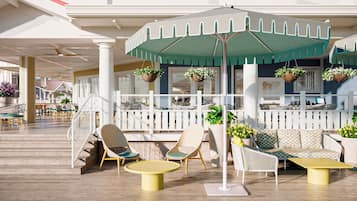 Un espace extérieur ensoleillé, aménagé avec des chaises en osier, une table jaune et un parasol vert.