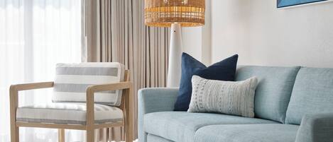 A living room with a light blue sofa, a wooden-framed chair, and a woven floor lamp.