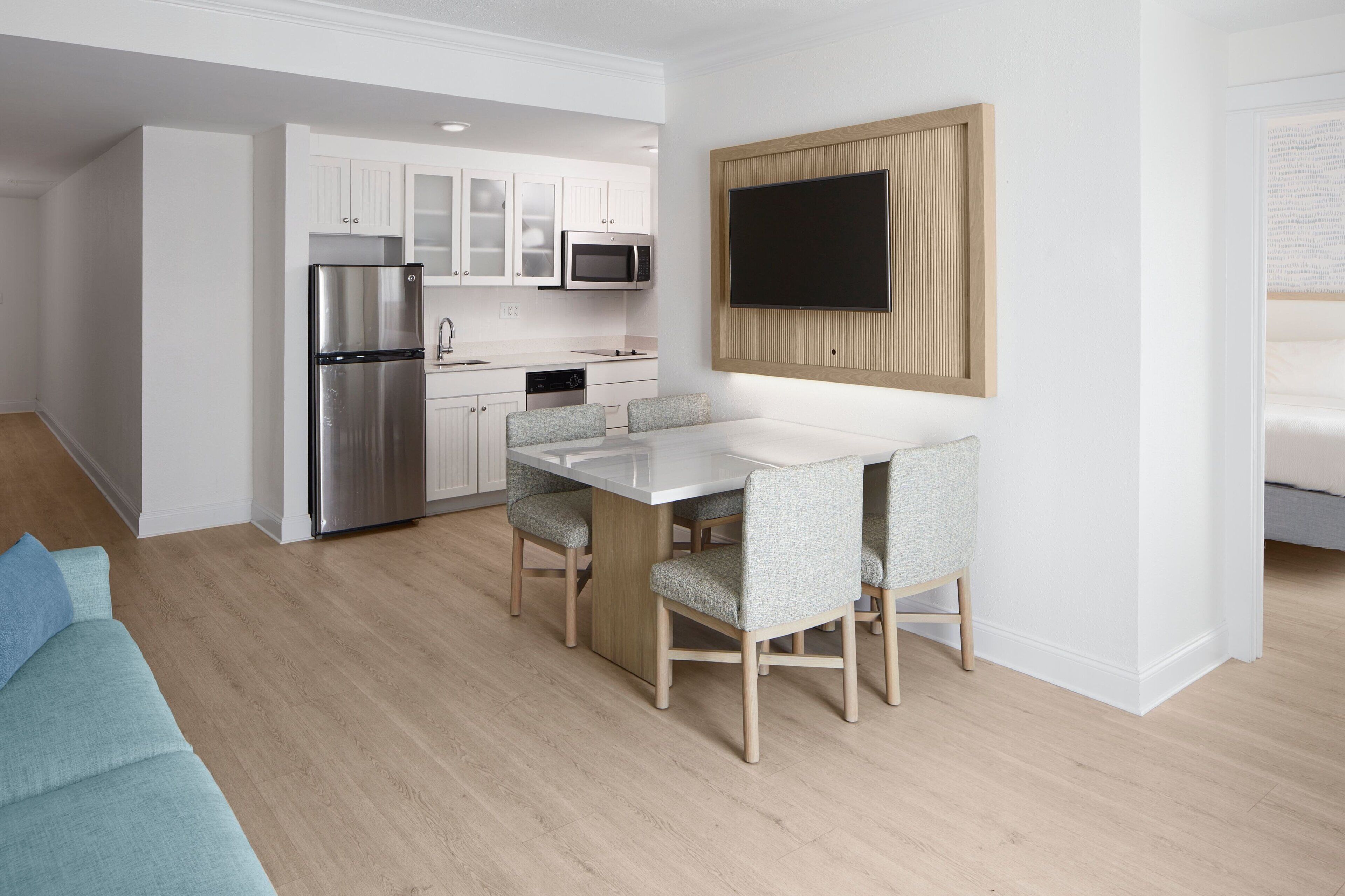 Une cuisine moderne avec des meubles blancs, des appareils en acier inoxydable et un coin repas comprenant une table blanche et des chaises grises.