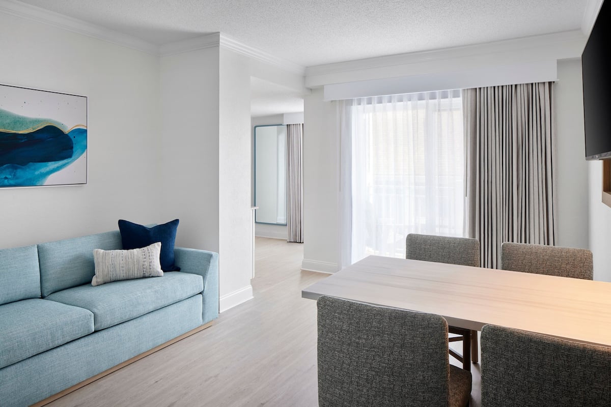 Ein modernes Hotelzimmer mit einem hellblauen Sofa, einem Holztisch und grauen Polsterstühlen.