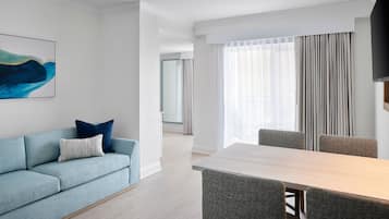 Una camera d'albergo moderna con un divano blu chiaro, un tavolo da pranzo in legno e sedie rivestite di grigio.