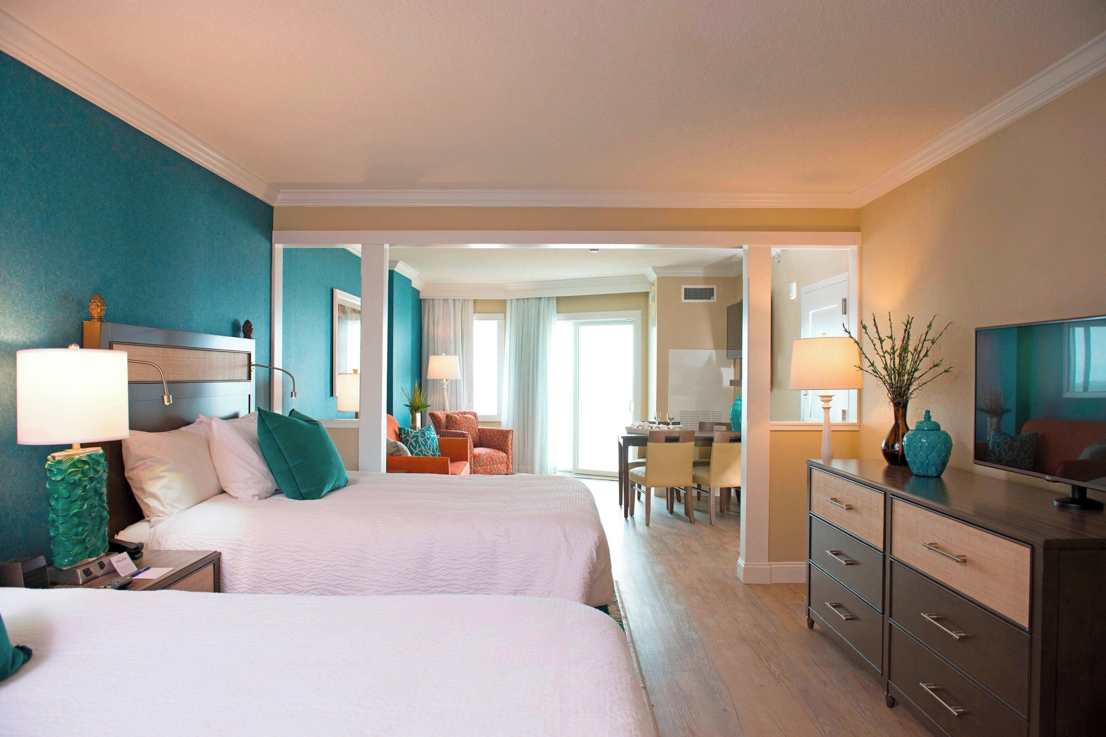 A hotel room with two beds, a desk, a chair, a dresser, and a television.