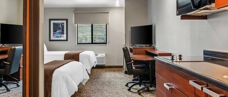 A hotel room with two beds, a desk, a chair, a microwave, and a television.