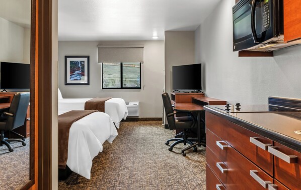 Une chambre d’hôtel avec deux lits, un bureau, une chaise, un four à micro-ondes et une télévision.