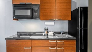 Une cuisine avec des meubles de rangement en bois, un réfrigérateur noir, un four à micro-ondes, une machine à café et un évier.
