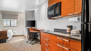Une chambre d’hôtel compacte comprenant un coin cuisine, un lit recouvert d’une housse blanche, un bureau avec une chaise et un téléviseur.