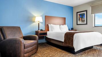 A hotel room with a bed, a chair, a nightstand with a lamp, and a picture on the wall.