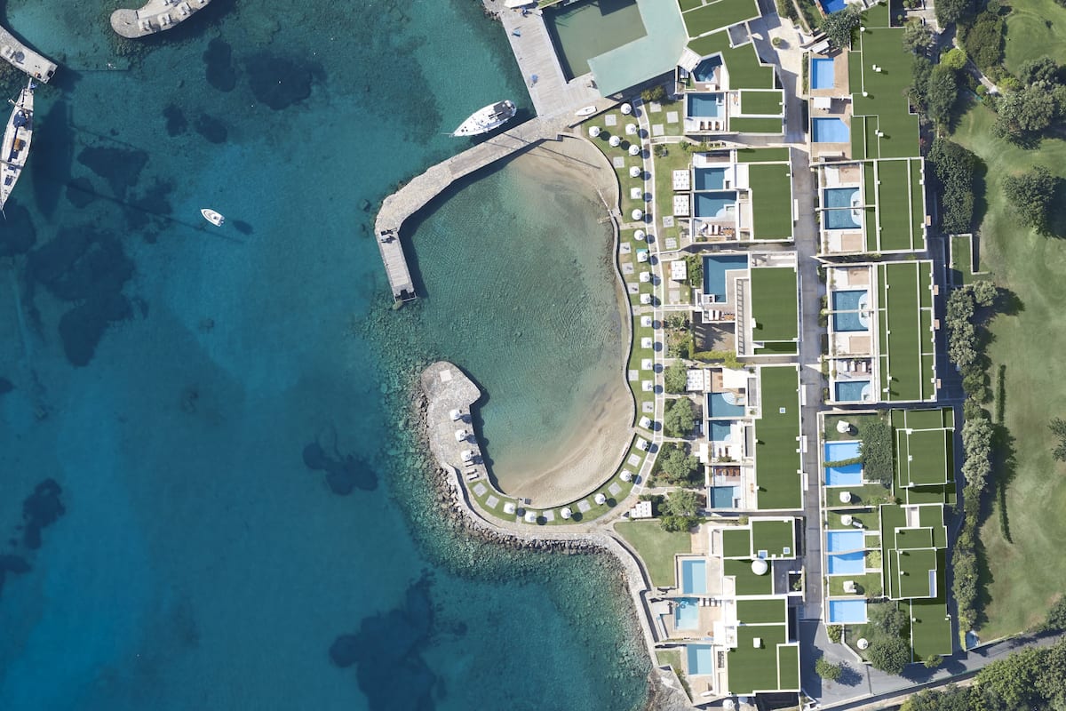 An aerial view of a coastal resort with multiple swimming pools, a marina, and a beachfront area.