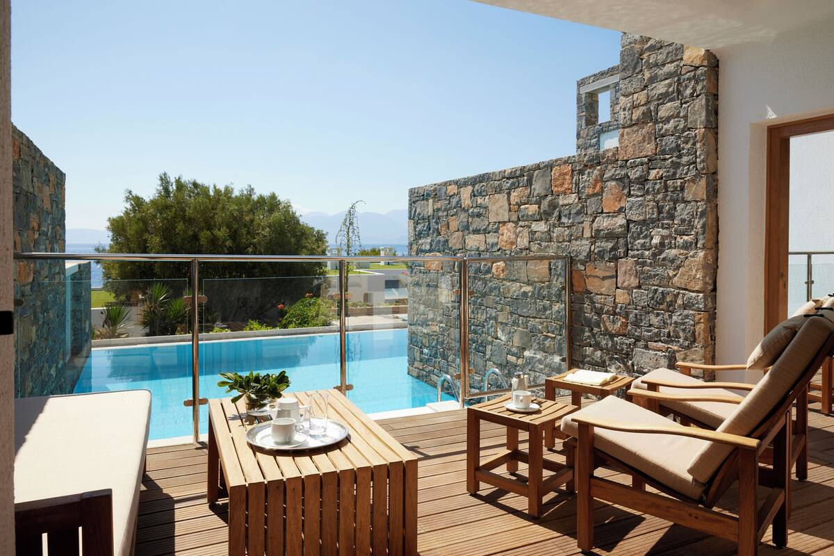 A wooden deck with a pool, stone walls, and lounge chairs.