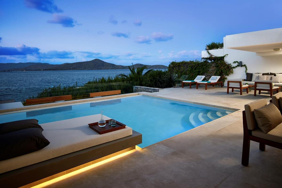 A poolside area with a view of the sea, lounge chairs, and a dining table.