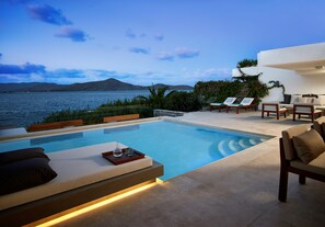 A poolside area with a view of the sea, lounge chairs, and a dining table. - Elounda Peninsula Luxury Resort (Agios Nikolaos)