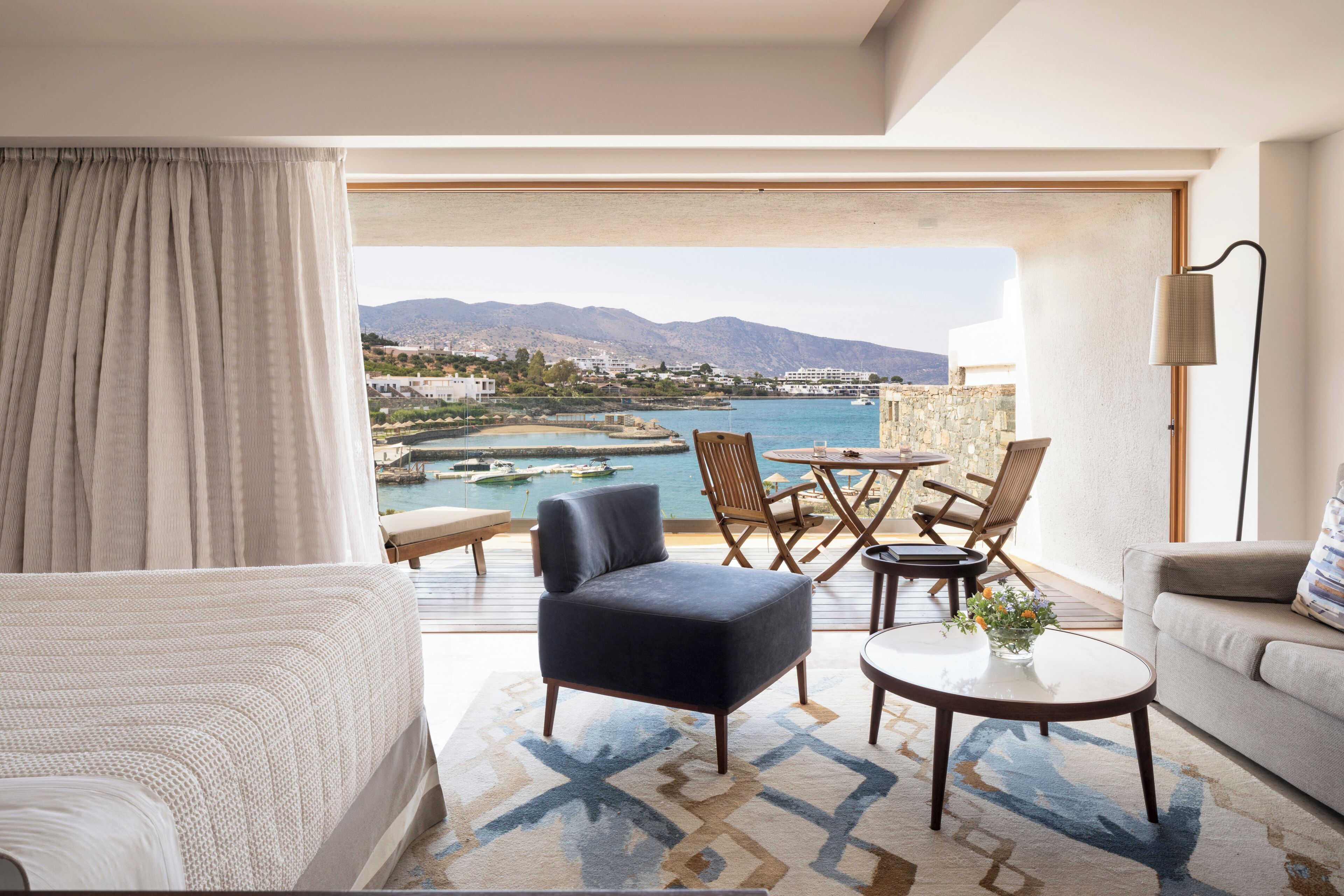 Habitación de hotel moderna con balcón y vistas panorámicas de la costa, que incluye un sofá, una silla, una mesita y una lámpara.