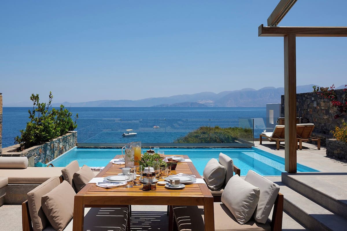 A poolside dining area with a table set for two, overlooking a sea view.