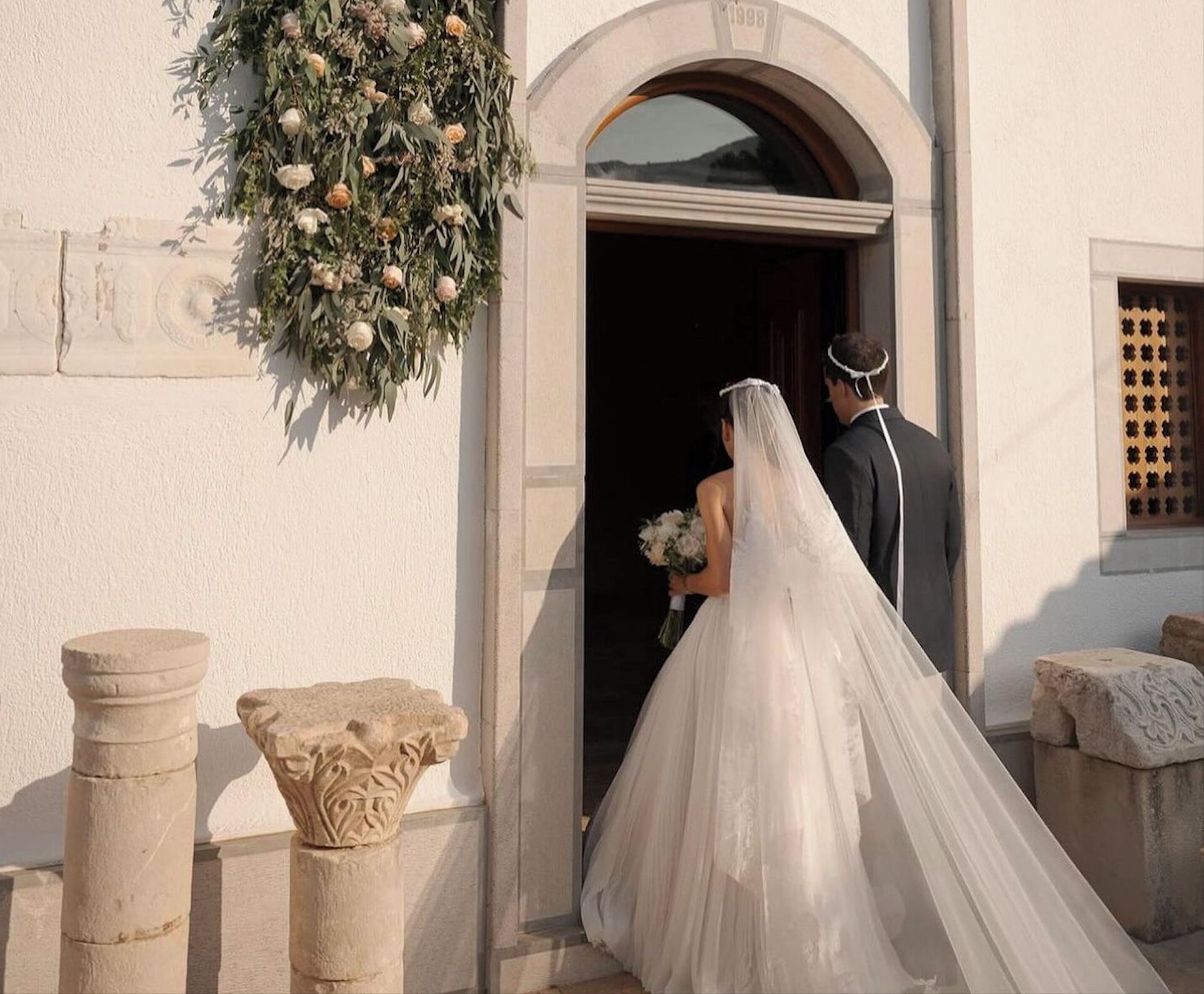 A wedding couple exiting a building with a floral decoration above the entrance.