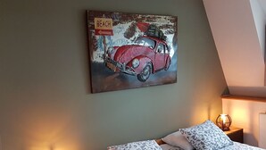 A bedroom with a bed, two bedside tables, a wall-mounted artwork of a red car, and a lamp on each table.