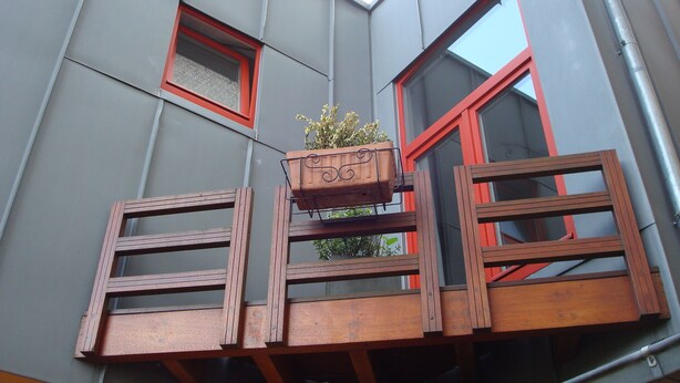 A modern building with a balcony, a window with a red frame, and a potted plant on the balcony.