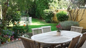 A round wooden table with six chairs, surrounded by potted plants and a small garden.